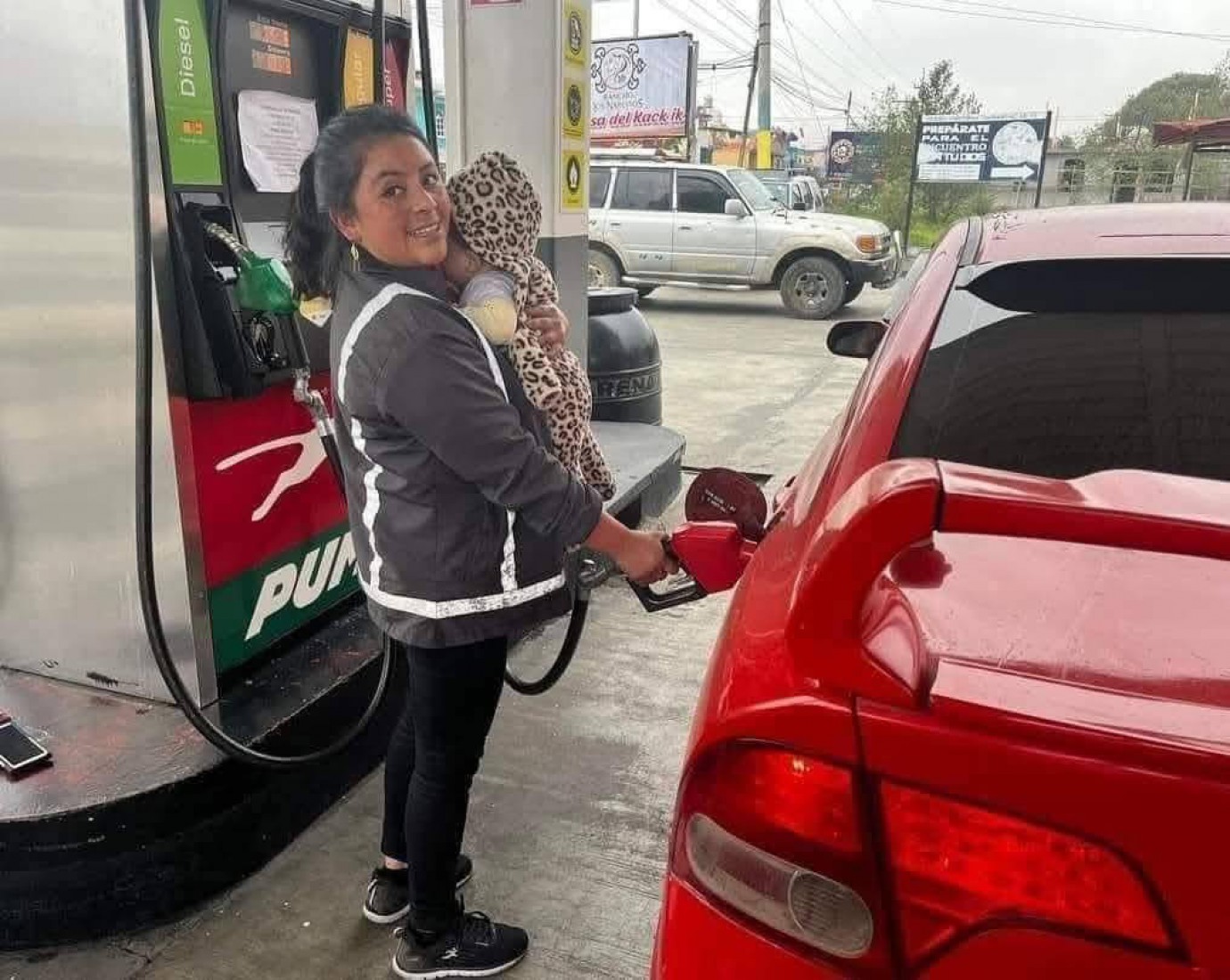 Una madre trabaja en una estación de servicio con su bebé en brazos