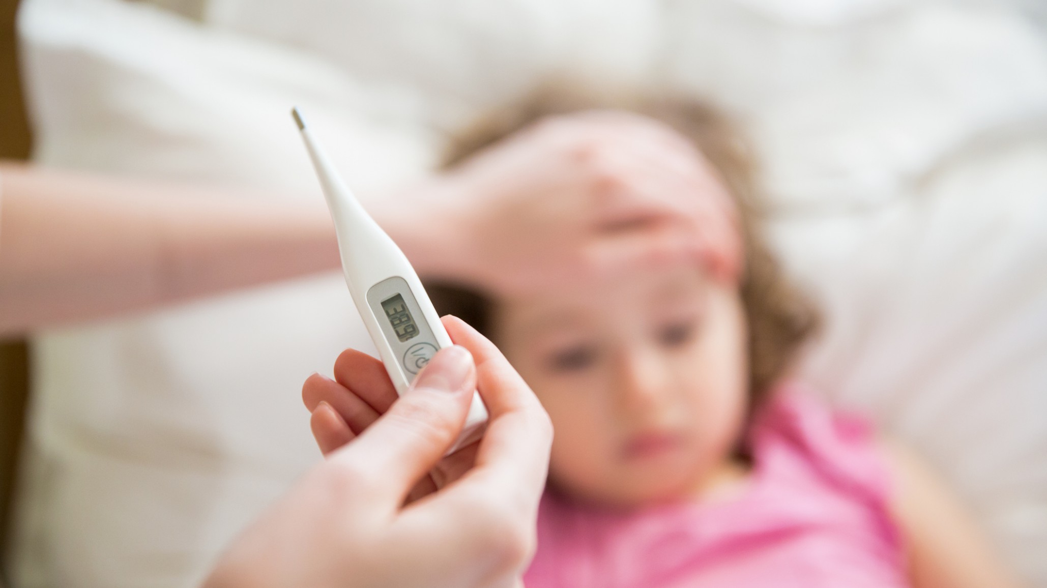 <p>Close-up thermometer. Mother measuring temperature of her ill kid. Sick child with high fever laying in bed and mother holding thermometer. Hand on forehead.</p>